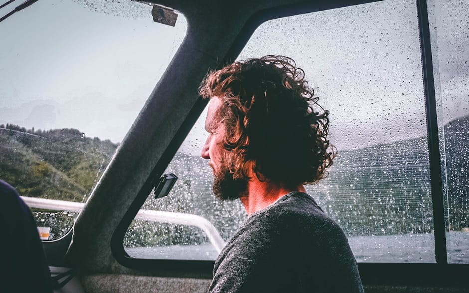 Side view of a man with facial hair on a rainy boat ride, looking thoughtful.